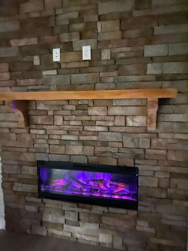 Stone fireplace wall with a timber mantel and accent lighting
